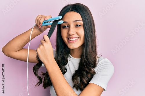 Young hispanic woman holding hair straightener smiling with a happy and cool smile on face. showing teeth.