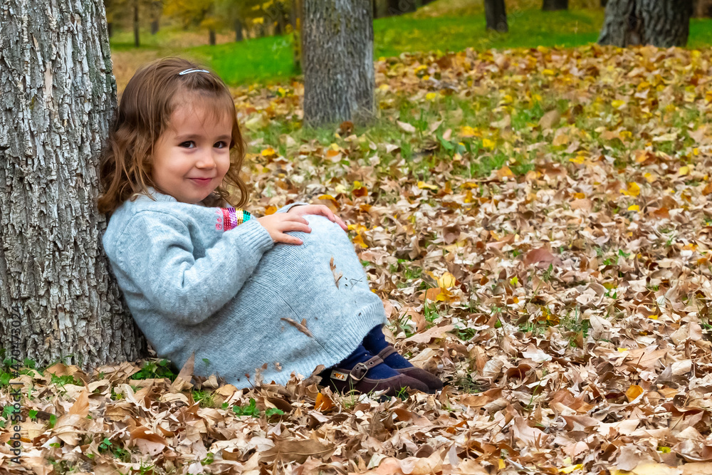 Little girl sitting on the forest floor leaning on a tree Little girl sitting on the forest floor leaning on a tree