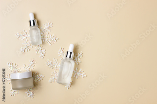 Cosmetic jars on a beige background with snowflakes. Winter care products. Cream, serum, fluid. Minimalism.