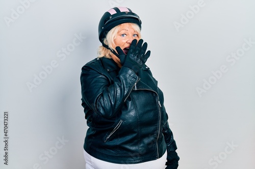 Middle age blonde woman holding motorcycle helmet bored yawning tired covering mouth with hand. restless and sleepiness.