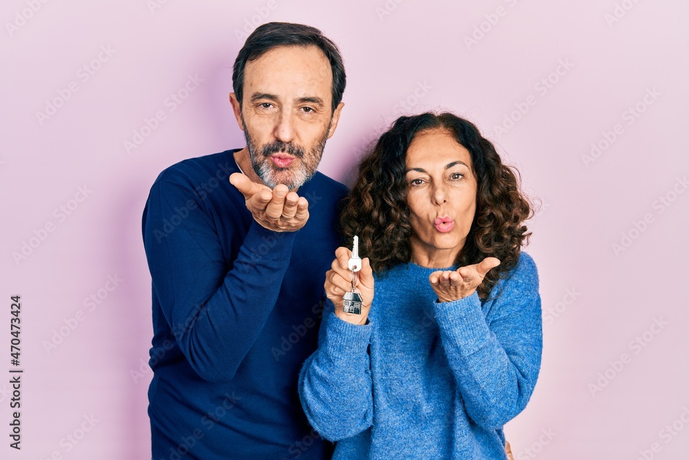 Middle age couple of hispanic woman and man holding keys of new home looking at the camera blowing a kiss with hand on air being lovely and sexy. love expression. Middle age couple of hispanic woman and man holding keys of new home looking at the camera blowing a kiss with hand on air being lovely and sexy. love expression.