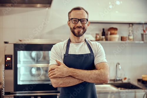 Photographie Cheerful bearded man in apron keeping arms crossed