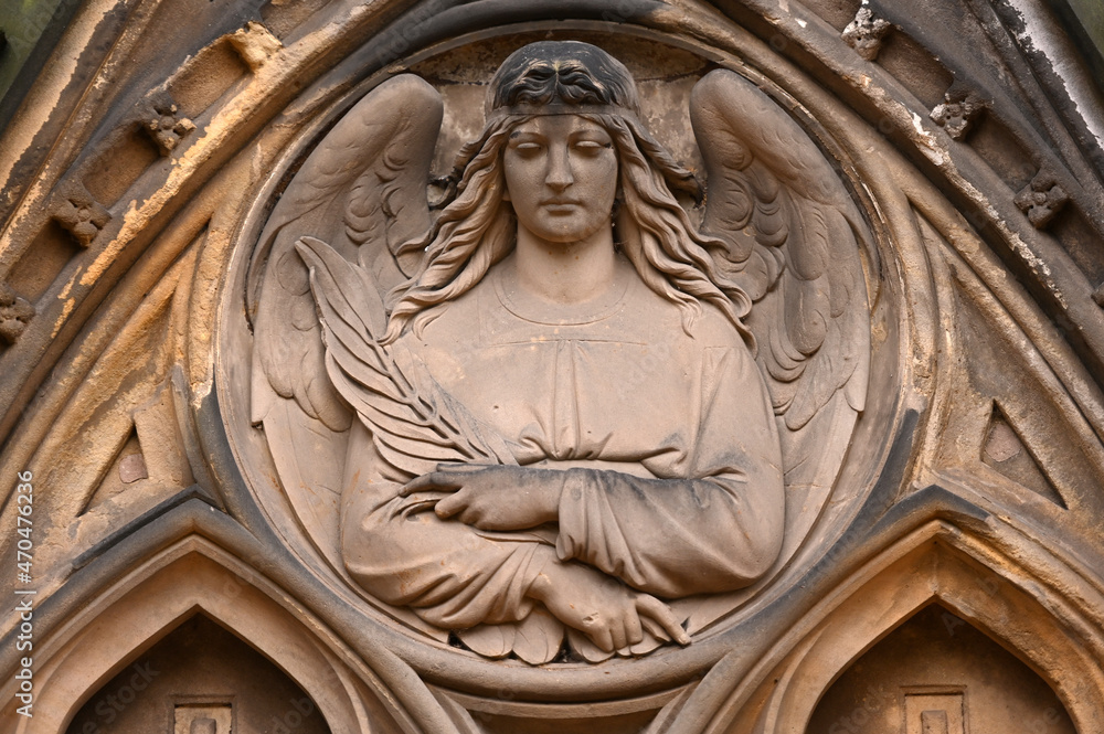 Partial view of a sandstone made angel holding a feather her hands.
