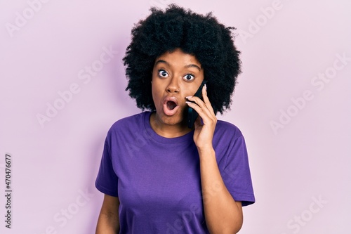 Young african american woman having conversation talking on the smartphone scared and amazed with open mouth for surprise, disbelief face