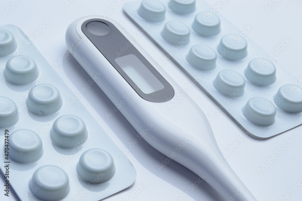 tablets in a package and a white electronic thermometer on a white surface close-up. tablets in a package and a white electronic thermometer on a white surface close-up.