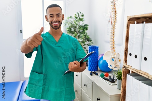 African american physiotherapist man working at pain recovery clinic approving doing positive gesture with hand  thumbs up smiling and happy for success. winner gesture.