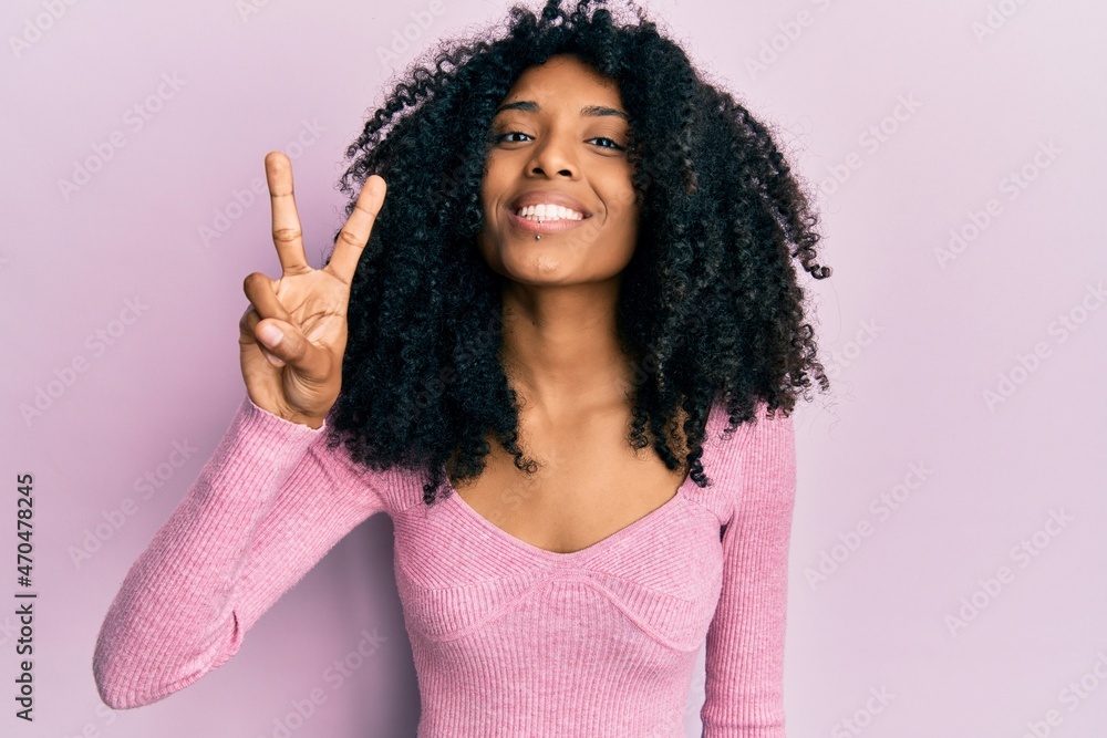 African american woman with afro hair wearing casual pink shirt showing and pointing up with fingers number two while smiling confident and happy. African american woman with afro hair wearing casual pink shirt showing and pointing up with fingers number two while smiling confident and happy.