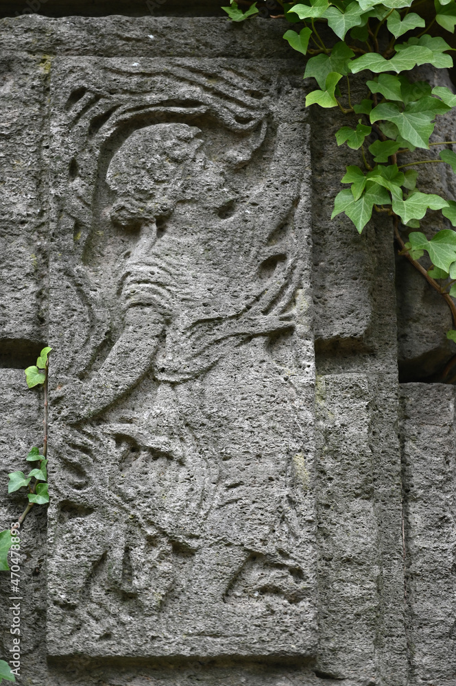 A weathered sandstone relief of a playing angel. A moss covered tombstone plate.