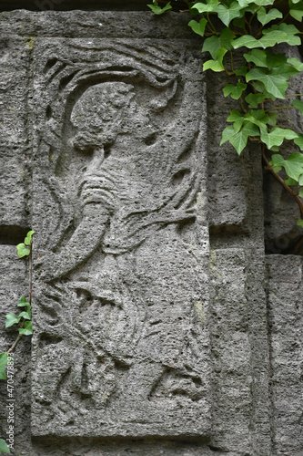 A weathered sandstone relief of a playing angel. A moss covered tombstone plate.