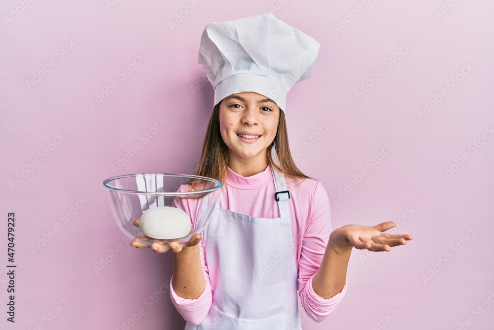 Beautiful brunette little girl wearing chef hat holding bread dough celebrating achievement with happy smile and winner expression with raised hand Beautiful brunette little girl wearing chef hat holding bread dough celebrating achievement with happy smile and winner expression with raised hand
