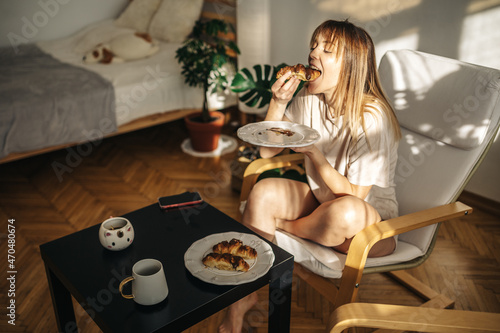 Attractive girl eating croissants in a bright room. Beautiful girl eating croissants with chocolate for breakfast