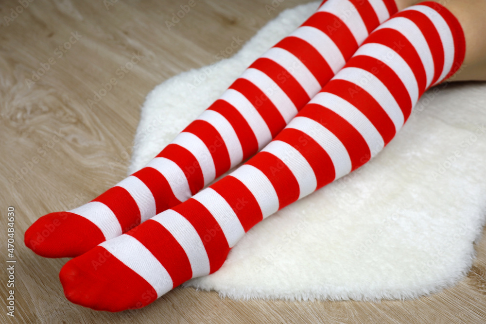 Girl in Christmas knee socks sitting on white fur rug on wooden floor. Female outfit for New Year celebration Girl in Christmas knee socks sitting on white fur rug on wooden floor. Female outfit for New Year celebration