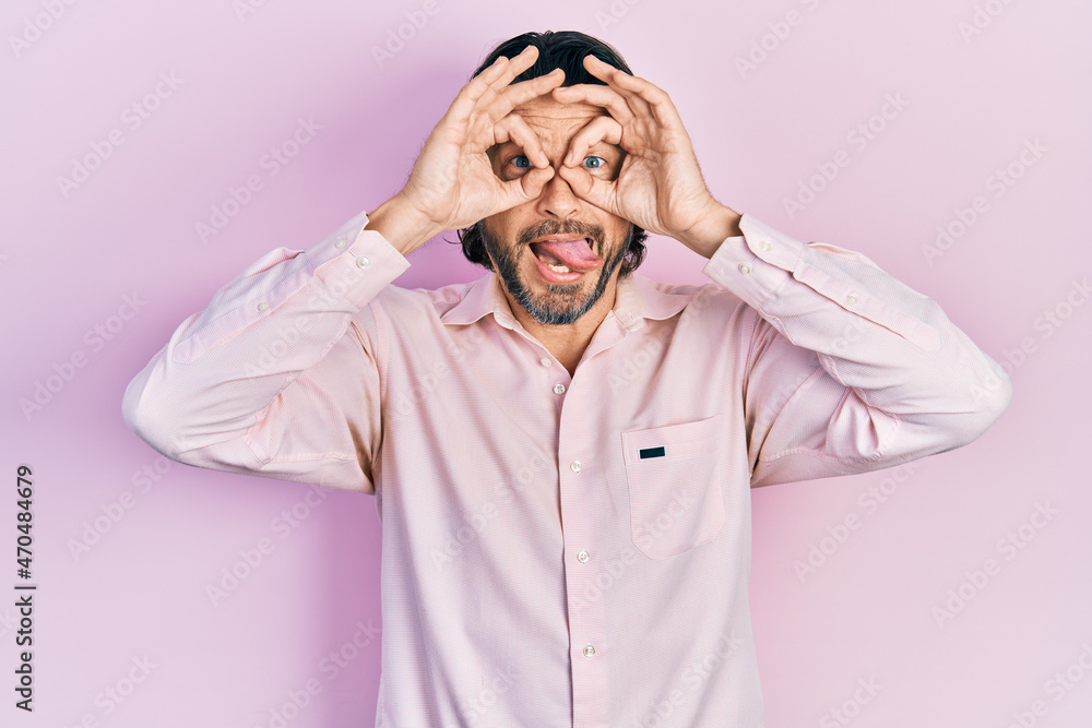Middle age caucasian man wearing casual clothes doing ok gesture like binoculars sticking tongue out, eyes looking through fingers. crazy expression.