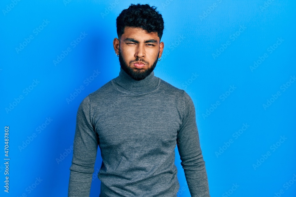 Arab man with beard wearing turtleneck sweater puffing cheeks with funny face. mouth inflated with air, crazy expression. Arab man with beard wearing turtleneck sweater puffing cheeks with funny face. mouth inflated with air, crazy expression.