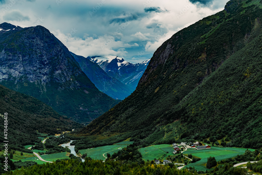 View from the road on a small village hidden in the valley between beautiful Norwegian mountains against  dramatic cloudy sky