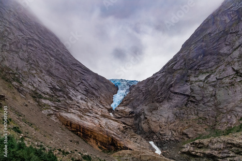 Scenic view on Briksdal glacier, and Norwegian mountains against cloudy dramatic sky