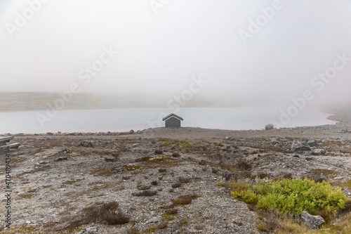 Mysterious view on the small house by the lake shore in the foggy landscape