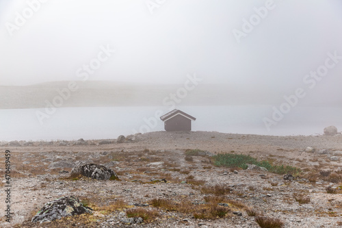 Mysterious view on the small house by the lake shore in the foggy landscape