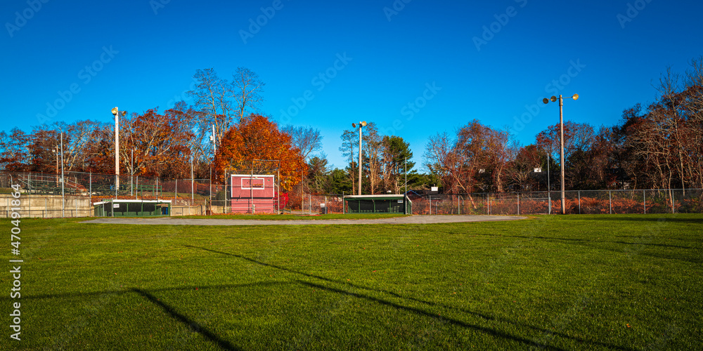 Baseball field with two dugouts, press box, stadium lights, and fence on blue sky background.