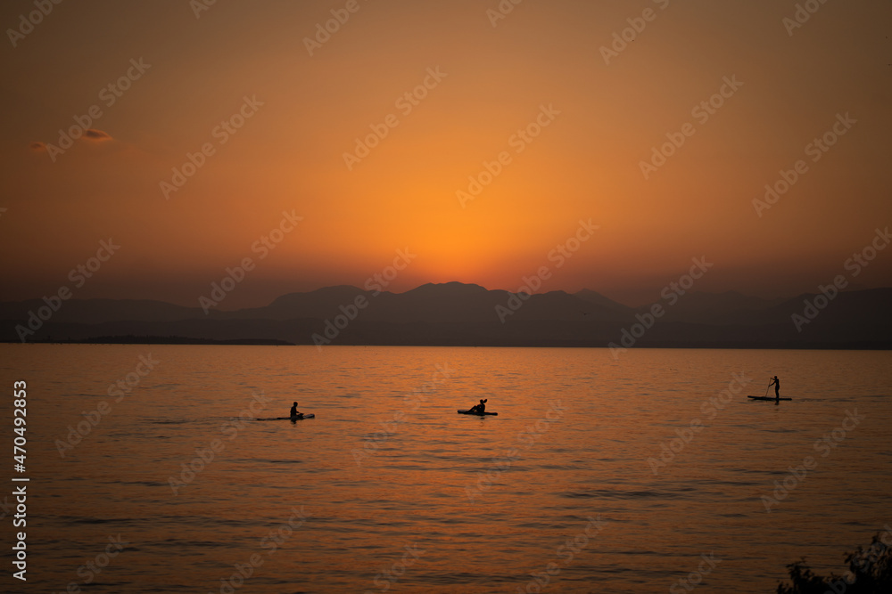People on a SUP enjoying the beautiful orange sunset at lake Garda in italy People on a SUP enjoying the beautiful orange sunset at lake Garda in italy