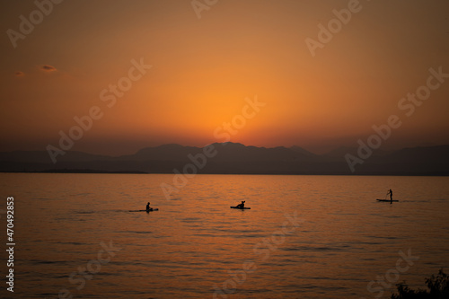 People on a SUP enjoying the beautiful orange sunset at lake Garda in italy 