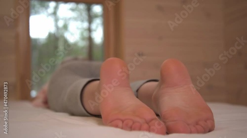 The child lies on the bed and looks out the window. Bare feet close-up. Healthy feet, no signs of flat feet.