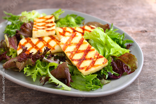 Green salad with fried halloumi cheese in a plate on a old wood background.