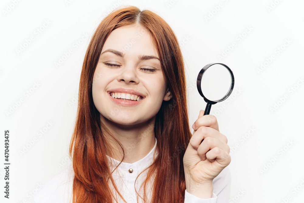 red-haired woman in a white shirt with a magnifying glass in her hands searching red-haired woman in a white shirt with a magnifying glass in her hands searching