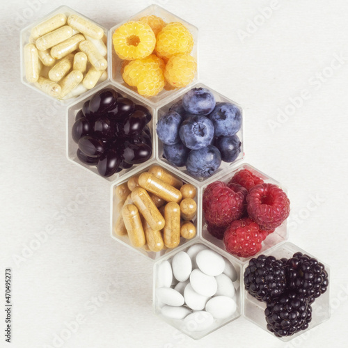 Fresh berries, pills and capsules in honeycomb like hexagonal jars