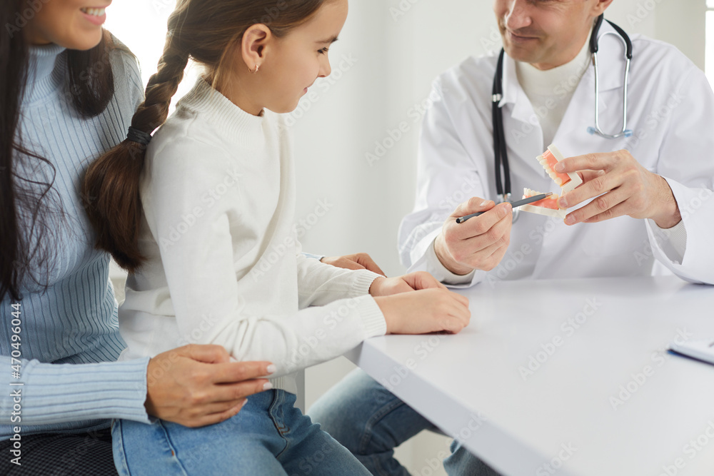 Obraz premium Close up of male dentist talk with mother and small daughter patients at consultation in clinic. Man doctor consult mom and child about oral hygiene and care. Dentistry, medicine concept.