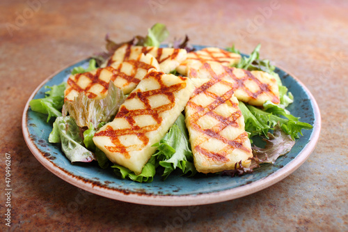 Green salad with fried halloumi cheese in a plate on a old background.