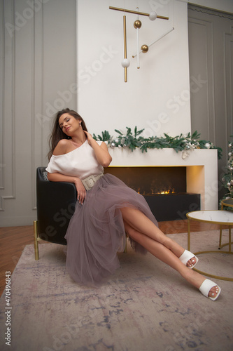 Young beautiful woman in white silk blouse and purple skirt posing in christams decorated interior