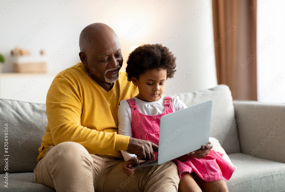 Happy african american small girl and grandfather surfing in internet or playing an online game on laptop Happy african american small girl and grandfather surfing in internet or playing an online game on laptop