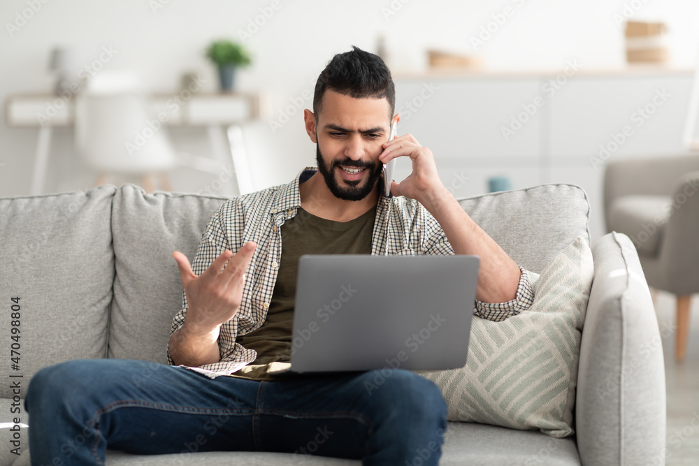 Handsome young Arab man calling on smartphone, using laptop for online meeting, working remotely from home Handsome young Arab man calling on smartphone, using laptop for online meeting, working remotely from home