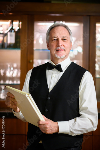 Portrait of a senor maitre in an elegant restaurant holding a couple of menus photo