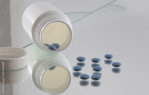 blue coated tablets in front of opened white plastic bottle