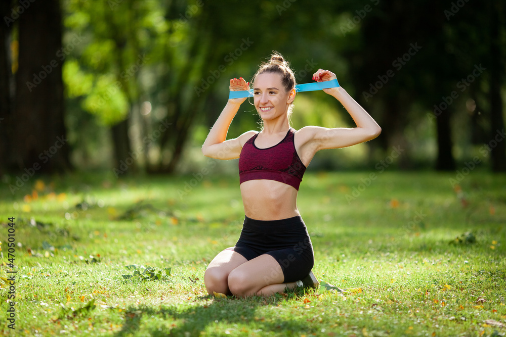 A girl on a sunny lawn in the park is engaged with a rubber band for her hands. Good mood during fitness. A girl on a sunny lawn in the park is engaged with a rubber band for her hands. Good mood during fitness.