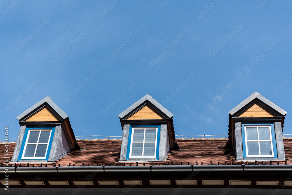 Old red roof and dormer windows on a blue sky.
