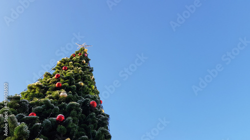 An elegant lonely Christmas tree decorated with garlands and a star against the blue sky. Outdoors, green decorated Christmas tree. As a background and texture for a holiday card with a place for text