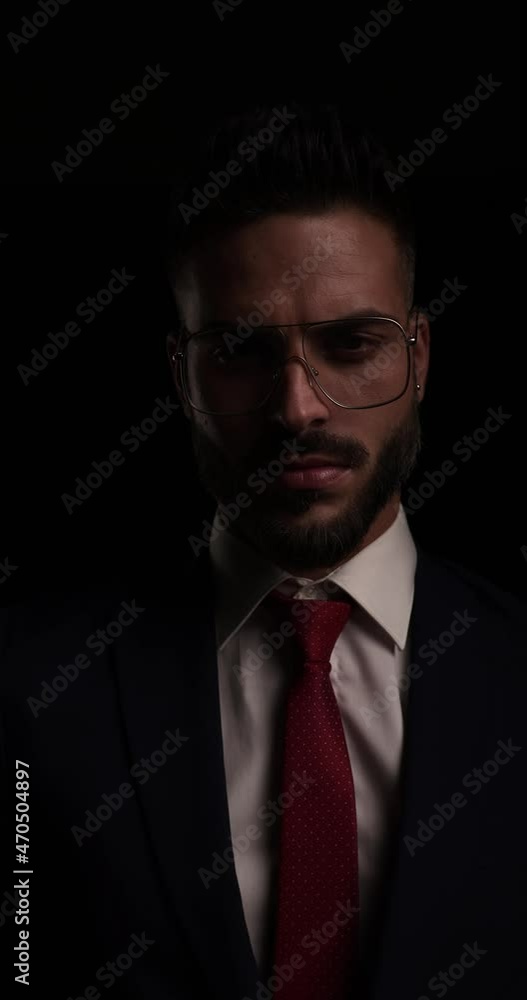 mysterious businessman with metal frame eyeglasses buttoning and closing suit, looking to side and crossing arms on black background in studio mysterious businessman with metal frame eyeglasses buttoning and closing suit, looking to side and crossing arms on black background in studio