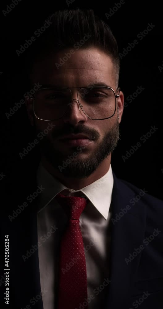vertical video of bearded young guy arranging and fixing metal frame glasses and suit, looking to side and crossing arms in the dark vertical video of bearded young guy arranging and fixing metal frame glasses and suit, looking to side and crossing arms in the dark