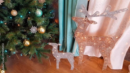 Screensaver with a green Christmas tree decorated with festive balls and a garland, as well as illuminated deer with antlers and a fawn. Background for the upcoming New Year and Christmas holidays.