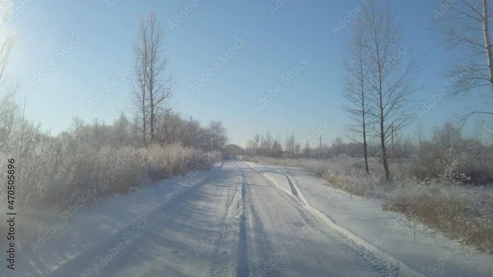 The car is driving on a snow-covered country road. The road is surrounded by snow-covered trees and grass covered with hoarfrost. View through the windshield of the car The car is driving on a snow-covered country road. The road is surrounded by snow-covered trees and grass covered with hoarfrost. View through the windshield of the car