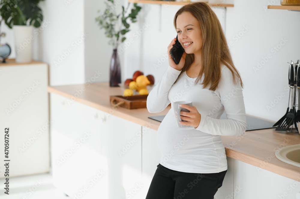 Beautiful pregnant woman drinks tea or coffee. Indoor photo.