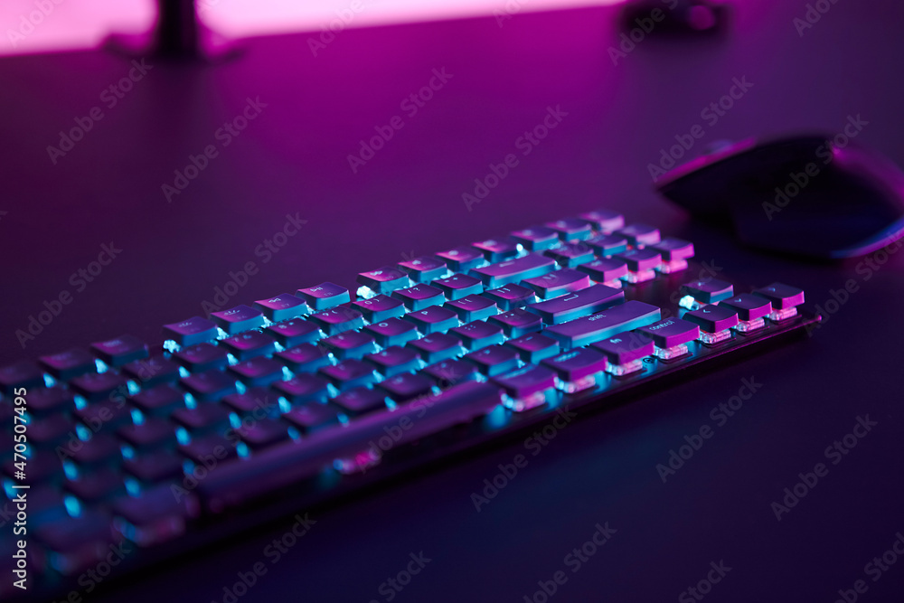 Computer mouse and illuminated keyboard laying on desk. Pink light in background. Computer mouse and illuminated keyboard laying on desk. Pink light in background.