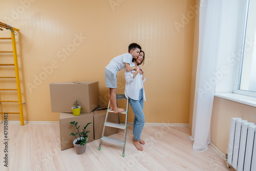 A young woman and her son are standing in front of the boxes and enjoying the housewarming after moving in. Housewarming, delivery and freight transportation, purchase of real estate. © Andrii
