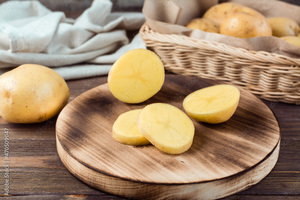 Fresh yellow potatoes cut into pieces on a board and a basket with tubers on a wooden table. Vegetarian food. Fresh yellow potatoes cut into pieces on a board and a basket with tubers on a wooden table. Vegetarian food.
