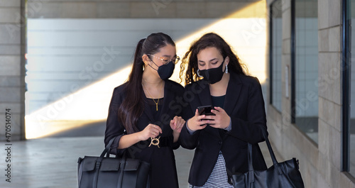 Dos mujeres de negocios con mascarilla consultan teléfono móvil photo