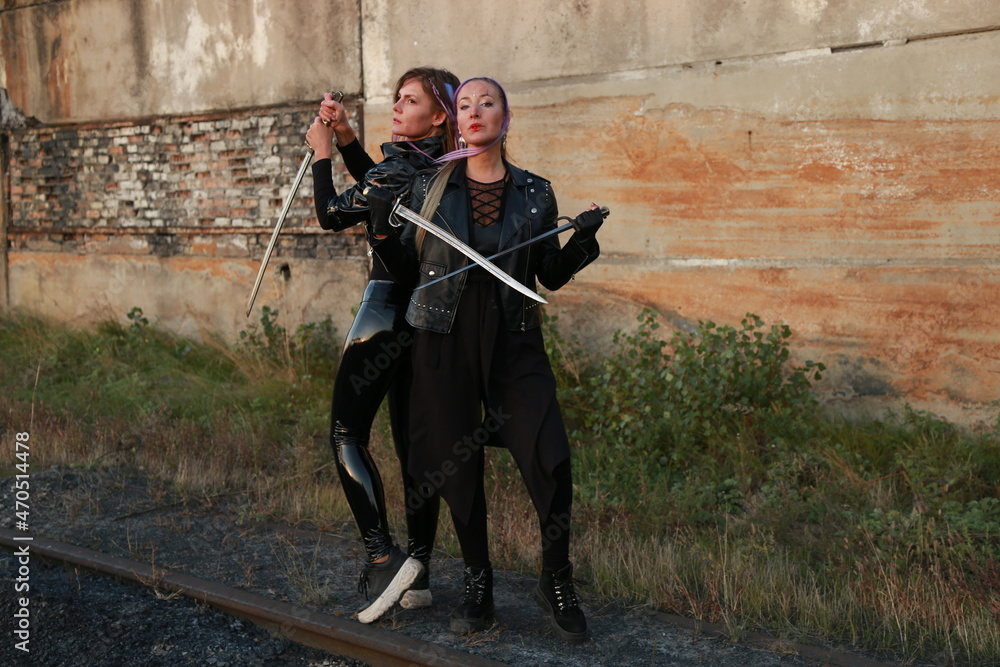 Naklejka premium Two warrior women in leather jackets with swords near vintage building