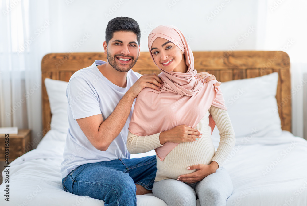 Happy expecting arab couple cuddling while spending time together at home, free space Happy expecting arab couple cuddling while spending time together at home, free space